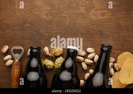 Eine Flasche Bier auf einem Teller mit gesalzenen Auberginen Brezeln, Pistaziennüssen und Chips auf einem schwarzen, zerkratzten Kreidetafel. Draufsicht. Hochwertiges Foto Stockfoto