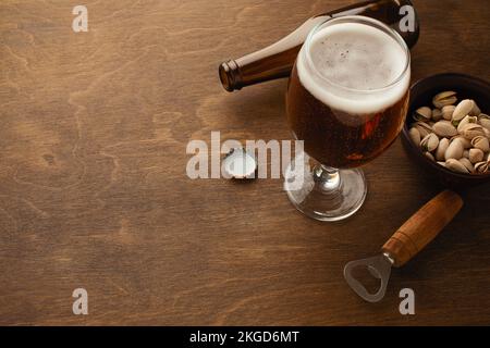 Eine Flasche Bier auf einem Teller mit gesalzenen Auberginen Brezeln, Pistaziennüssen und Chips auf einem schwarzen, zerkratzten Kreidetafel. Draufsicht. Hochwertiges Foto Stockfoto