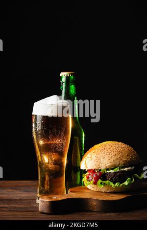 Eine Flasche Bier mit grünem Hopfen, Hafer, Weizenspikelets, Öffner und Gläser mit dunklem und hellem Bier auf schwarzem, zerkratztem Kreidetafel. Draufsicht. Hohe Qualität Stockfoto