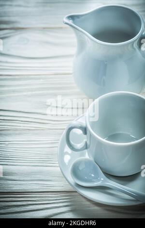 Keramiktasse Untertasse Teelöffel Milchkanne auf Holzbrett. Stockfoto