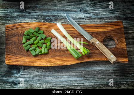 Gehackte Zwiebelstiele und Küchenmesser auf Holzbalken mit altem Holzhintergrund Stockfoto