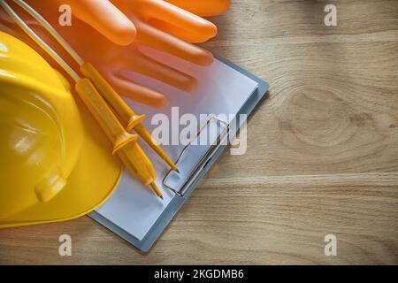 Klemmbrett Papier Bauhelm dielektrische Handschuhe elektrischer Tester auf Holzbrett. Stockfoto