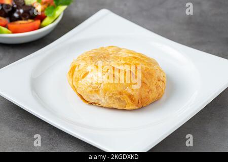 Türkischer Boyoz mit Oliven, Gurken und Tomaten daneben auf einem dunklen Steintisch Stockfoto