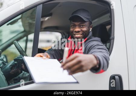 Junger erwachsener schwarzer Liefermann in rotem Pullover, der in einem weißen Lieferwagen lacht und Papiere an den Kunden hält, um von sget unterschrieben zu werden. Lieferservice. Horizontalschuss. Hochwertiges Foto Stockfoto