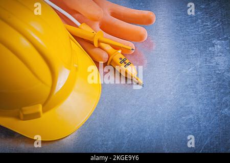 Isolierhandschuhe aus Gummi Bauhelm Elektrotester auf metallischem Hintergrund Elektrokonzept. Stockfoto