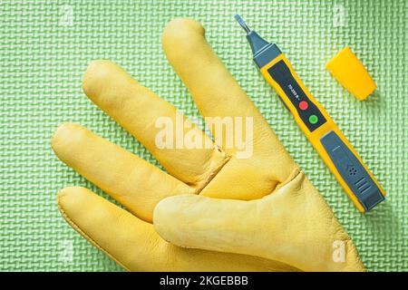 Lederschutzhandschuh elektrischer Tester auf grüner Oberfläche Stromkonzept. Stockfoto