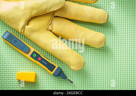 Elektrotester mit Lederschutzhandschuh auf grünem Hintergrund Stromkonzept. Stockfoto