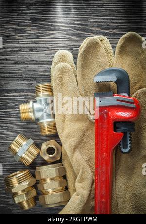 Sanitärarmaturen Rohrverschraubungen Sicherheitshandschuhe auf Holzbrett. Stockfoto