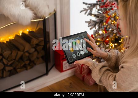Junge Frau verwendet Anwendung in seinem Smart Home zu Weihnachten Stockfoto