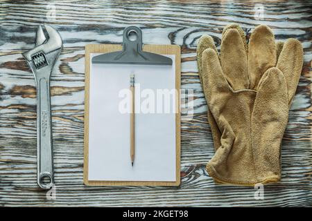 Schutzhandschuhe verstellbarer Schraubenschlüssel Bleistiftklemmbrett auf Holzbrett. Stockfoto