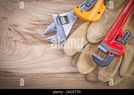 Schutzhandschuhe verstellbarer Schlüsselaffenschlüssel Rohrschneider auf Holzplatten Sanitärkonzept. Stockfoto