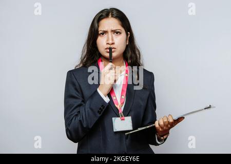 Verwirrte Unternehmensfrau, die eine Entscheidung erwägt – Stift an die Lippen, überraschter Büroausdruck. Überraschte weibliche Profis, die auf Unakzeptierte reagieren. Stockfoto