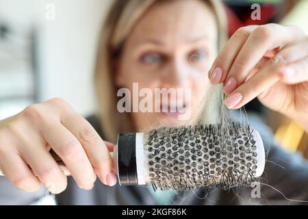 Haarausfall-Problem und ungesundes Haar. Frustrierte und verängstigte Frau, die einen Kamm mit viel Haar hält. Stockfoto