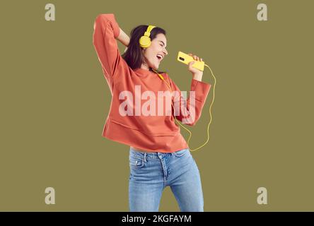 Brünette Frau in rotem Sweatshirt und Jeand, die Musik mit gelbem Smartphone und Headset hört. Stockfoto