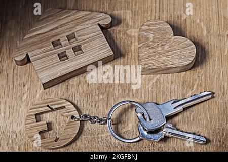 Ein Haus mit Schlüsseln und Herz auf Holzhintergrund Stockfoto