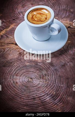 Vertikaler Blick auf Capuchino in weißer Kaffeetasse auf altem Holzquerschnitt des Baumstamms Stockfoto
