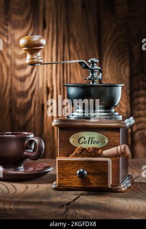 Vertikale Ansicht alte Holzkaffeemühle mit kleiner Schaufel und Tasse auf Holzhintergrund Stockfoto