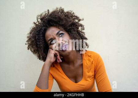 Junge Erwachsene afrikanerin, die an etwas denkt, nachdenklicher Ausdruck einer Afro-Frisur-Frau, stylisches Make-up Stockfoto