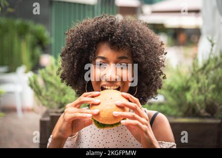 Junge afrikanische Frau genießt vegetarischen Burger im Restaurant, gesundes Essen und neues Konzept von Abits und Fütterung Stockfoto