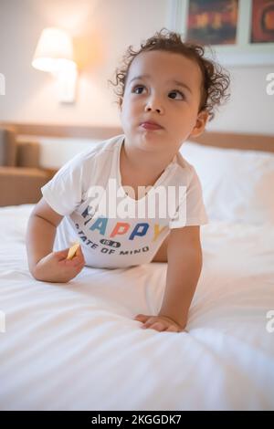 Der kleine Junge liegt auf dem Bauch auf einem weißen Bett im Hauptschlafzimmer Stockfoto