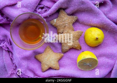 Eine Tasse Tee mit Zitrone und Keksen auf einem Winterschal. Stockfoto