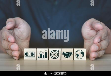 Nahaufnahme eines Mannes, der Holzwürfel mit verschiedenen geschäftsbezogenen Ikonen präsentiert - Entwicklungskonzept Stockfoto