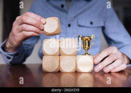 Geschäftsmann, der große Holzblöcke mit einer Siegertrophäe arrangiert. Geschäftserfolg Stockfoto