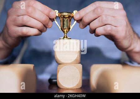 Geschäftsmann, der große Holzblöcke mit einer Siegertrophäe arrangiert. Geschäftserfolg Stockfoto