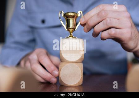 Geschäftsmann, der große Holzblöcke mit einer Siegertrophäe arrangiert. Geschäftserfolg Stockfoto