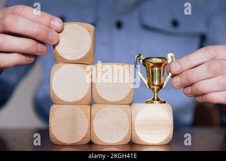 Geschäftsmann, der große Holzblöcke mit einer Siegertrophäe arrangiert. Geschäftserfolg Stockfoto