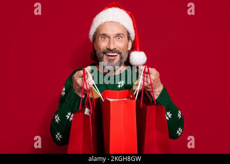 Porträt eines lustigen, aufgeregten Mannes, lächelnde Hände halten festliche Ladenpakete isoliert auf rotem Hintergrund Stockfoto