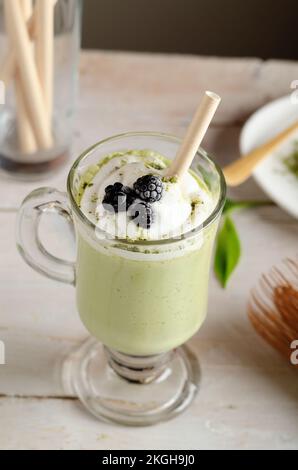 Nahaufnahme von Matcha Latte mit Schlagsahne und Blaubeeren in Glas auf hellem Hintergrund. Stockfoto