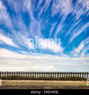 Normaler Betonzaun gegen blauen Himmel und schräge Zirruswolken Stockfoto