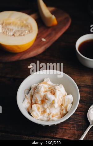 Hausgemachte Eiscreme gemischt mit Honigmelone und Süßsirup in klassischer Schüssel und Tasse Kaffee auf Holztisch Stockfoto