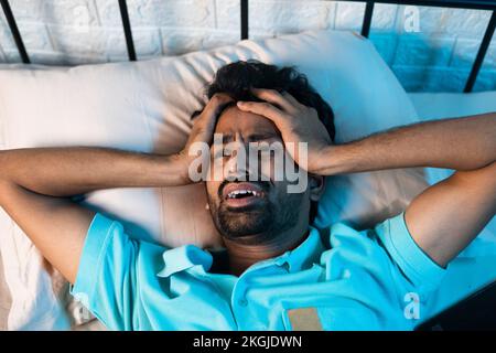 Schreiender junger Mann mit Schlaflosigkeit oder Schlaflosigkeit in der Nacht im Schlafzimmer - Konzept von Drogenabhängigen, Migräne und Stress Stockfoto