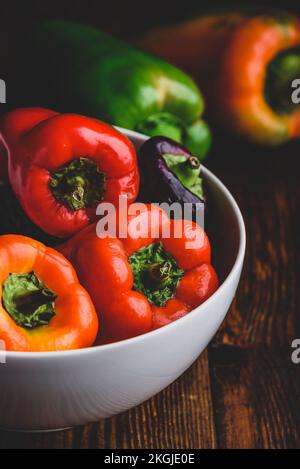 Bunte, frische Paprika in einer Schüssel auf einem Holzhintergrund Stockfoto