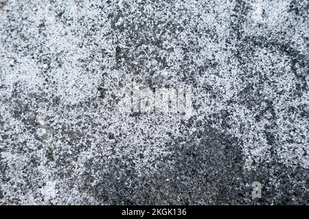 Salz verteilt auf eisigen Pflaster in der Stadt. Ziegel mit Salzflecken bedeckt. Rutschiger Gehweg im Winter. Stockfoto