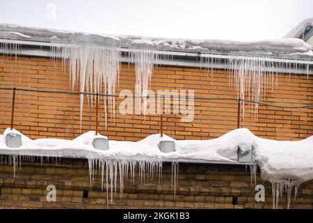 Scharfe Eiszapfen, die am Rand des Dachs hängen. Schmelzender Schnee bildet Eiszapfen. Stockfoto