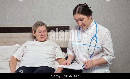 Der Arzt macht Notizen, wenn er Beschwerden einer Patientin hört Stockfoto