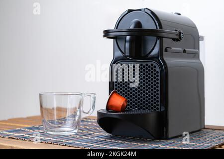 Stillleben von erfrischenden Espresso Kapsel und Tasse neben der Kaffeemaschine innen zu Hause. Niemand Stockfoto