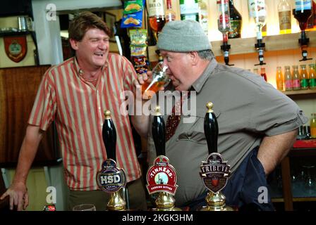 Auf dem Set „Doc Martin“ mit Martin Clunes (im Anzug), Ian McNeice (Hut) und John MacNeill (gestreiftes Hemd). Clunes wurde von Tomatensoße getäuscht Stockfoto