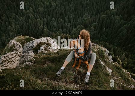 Eine Frau, die mit Vizsla Dog am Berggipfel sitzt Stockfoto