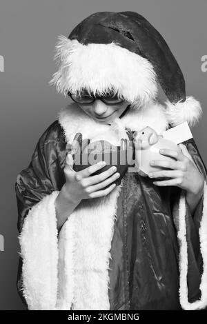 Junge süße weihnachtsmann Junge mit Gläsern in rotem Pullover und Neujahr weihnachtshut mit rosa Schweinebank und Schokolade Hip Cookies in Schüssel auf Stockfoto