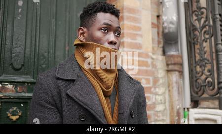 Junger schwarzer Mann, der während der Wintersaison nach draußen geht. Ein Afrikaner verlässt sein Haus am Anfang des Tages Stockfoto