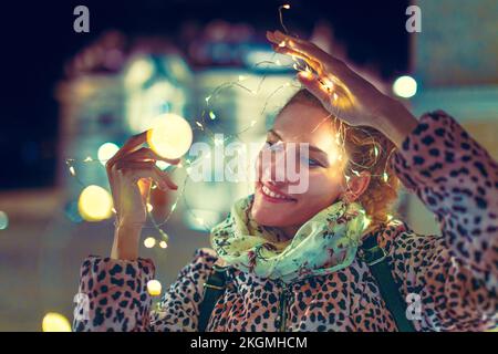 Glückliche junge weiße Frau, die im Winter mit LED-Girlande spielt Stockfoto