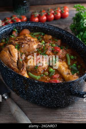 Brauner Hühnereintopf mit Gemüse, Kartoffeln und Hülsenfrüchten in einem altmodischen Topf auf einem Holztisch Stockfoto