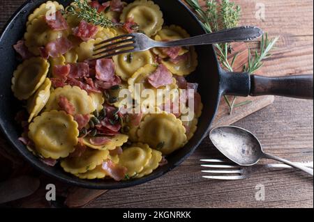 Italienisches Nudelgericht mit Ravioli und Pilzfüllung. Gekocht mit Butter, Schinken, Kräutern und gerösteten Kürbiskernen Stockfoto