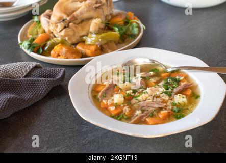 Teller mit frisch zubereiteter Hühnchen-Nudelsuppe mit alphabetischer Pasta auf dem Küchentisch Stockfoto