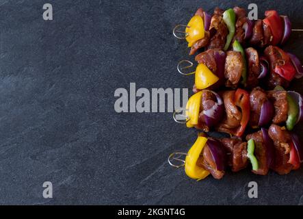 Schaschlik-Spieße mit roten, grünen und gelben Paprika, roten Zwiebeln und mariniertem Schweinefilet, isoliert auf dunklem Hintergrund Stockfoto