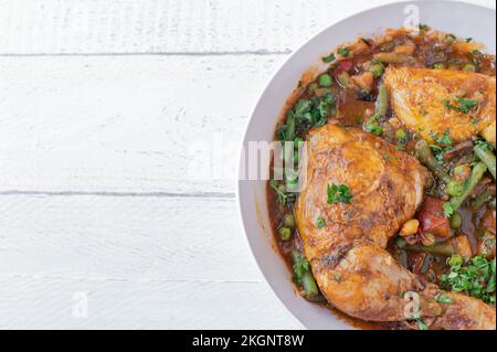 Geschmorte Hähnchenschenkel mit Gemüse, Kartoffeln und Hülsenfrüchten in einer Schüssel, isoliert auf weißem Hintergrund. Seitenansicht mit Kopierbereich Stockfoto